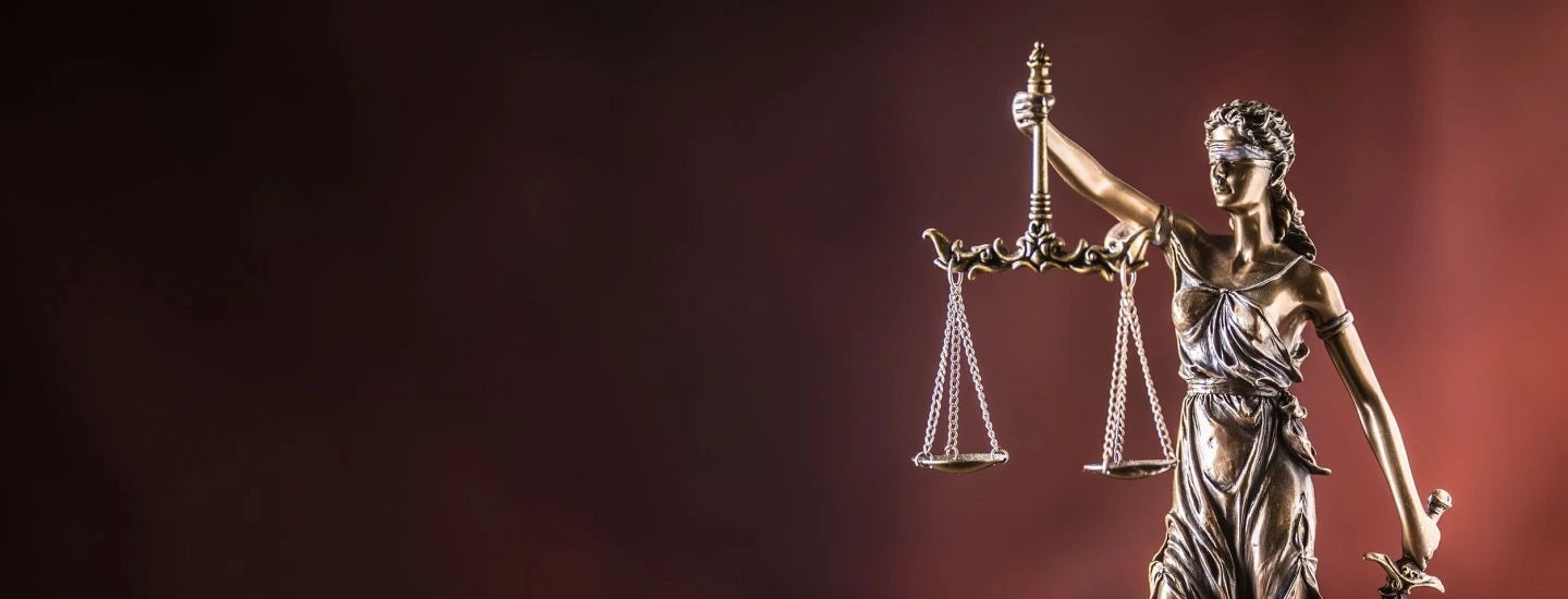 Lady Justicia holding sword and scale bronze figurine on wooden table.