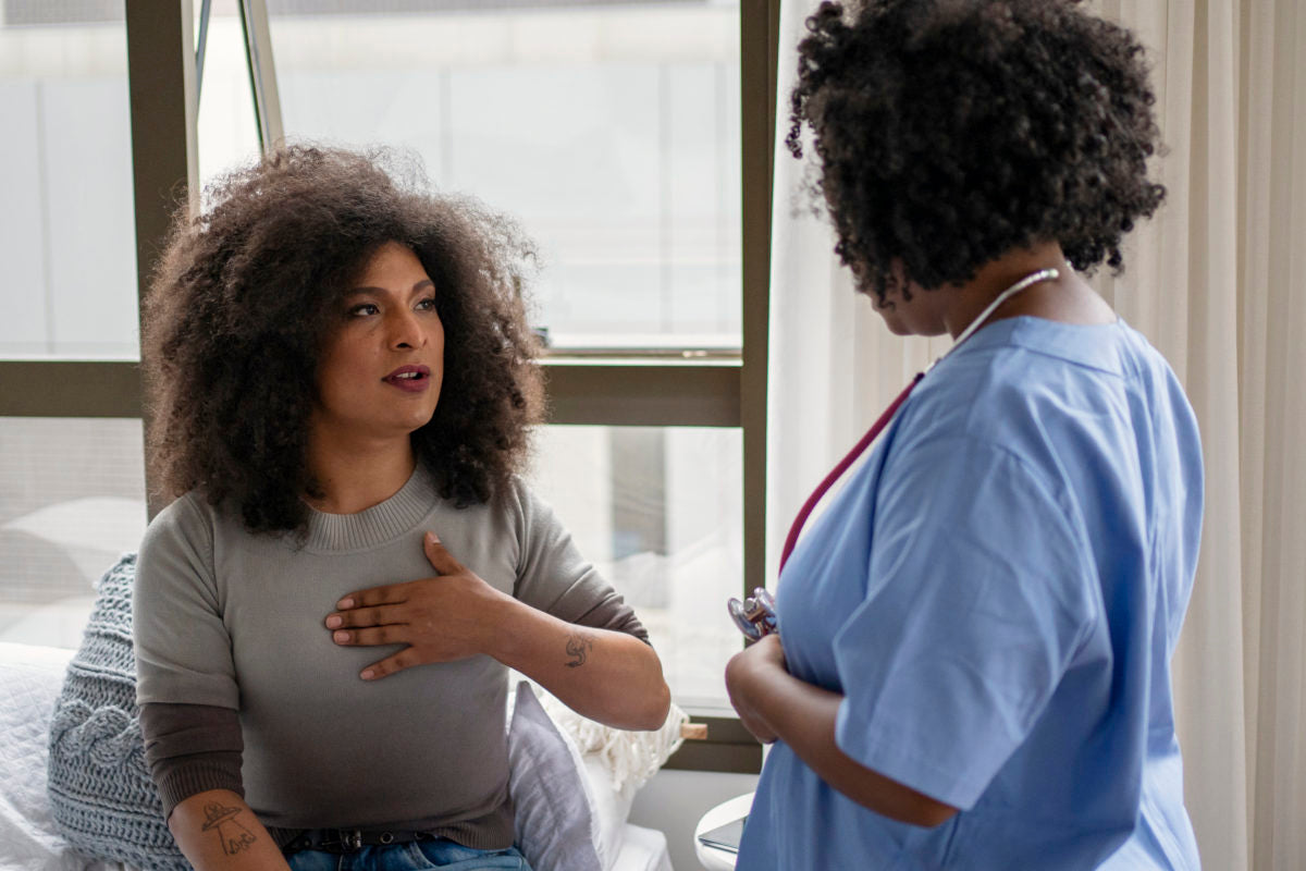 A seated patient describes their symptoms to a nurse standing beside them and wearing a stethoscope