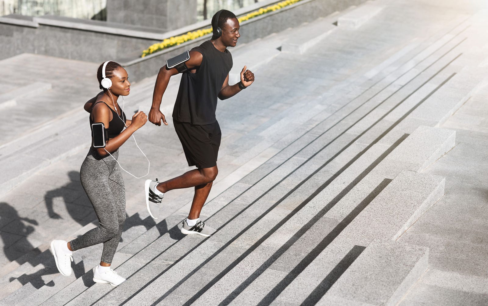 a man and woman wearing headphones jogging up steps outdoors