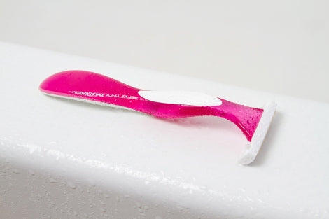 A pink razor sits on the edge of a bathtub